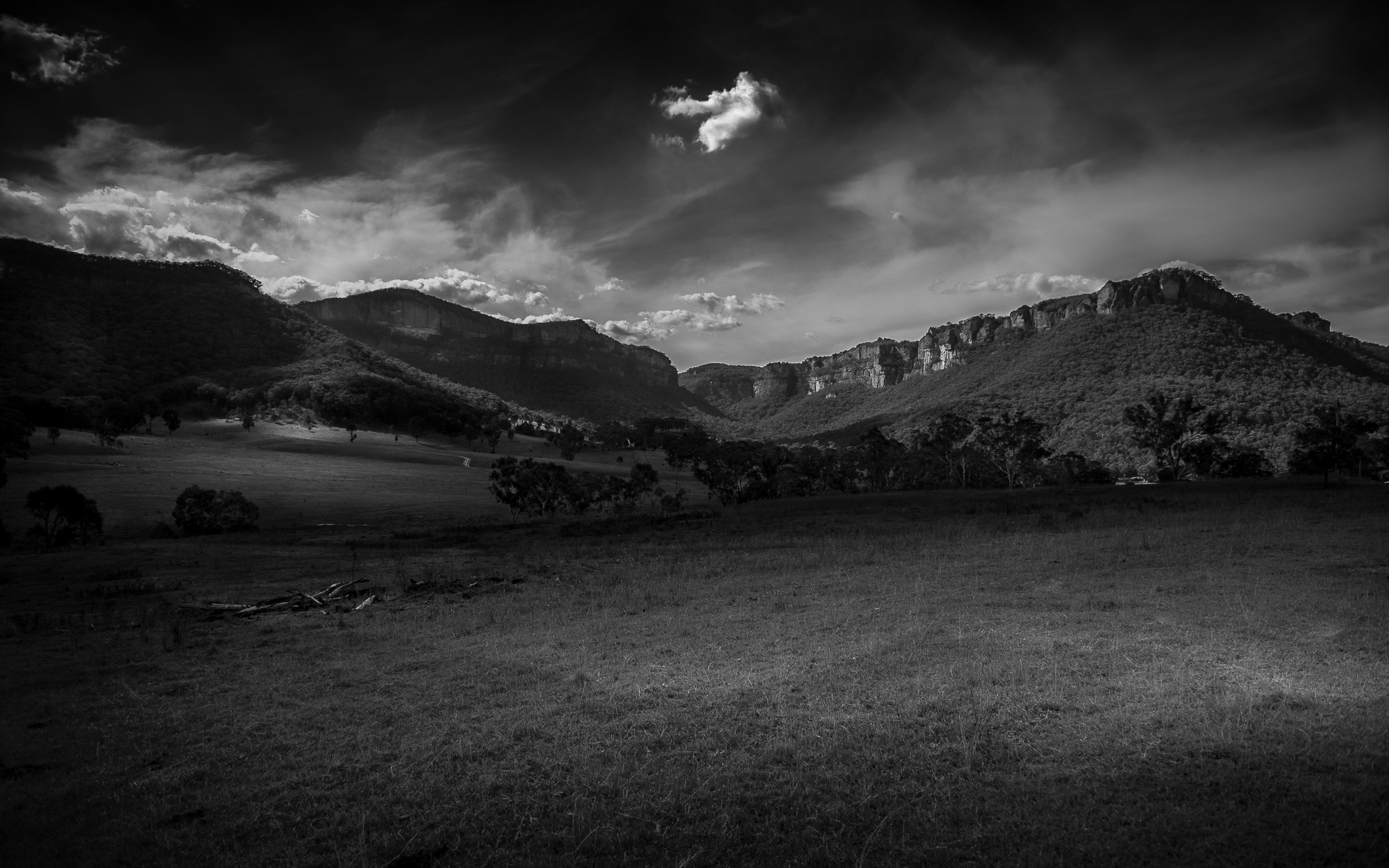 Dark and moody black and white landscape photograph showing mountain range surrounding rolling farmland